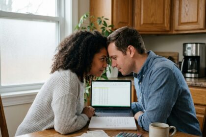 Couple gérant leur budget commun ensemble à la table de cuisine avec un ordinateur portable et des documents financiers